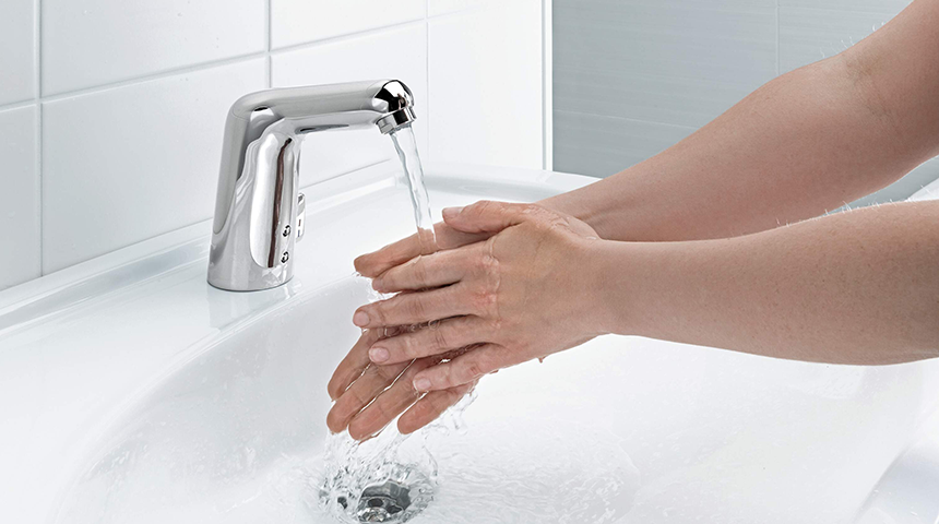 Person wäscht im Badezimmer Hände an einer berührungslosen Armatur.